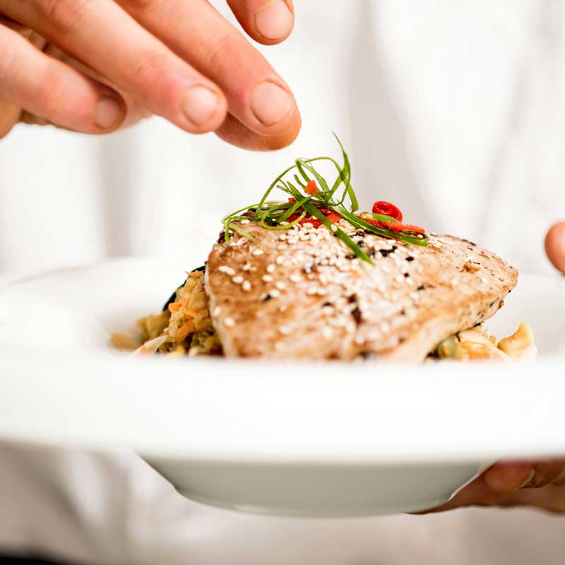A close up photo of a chef adding garnish to a plated meal