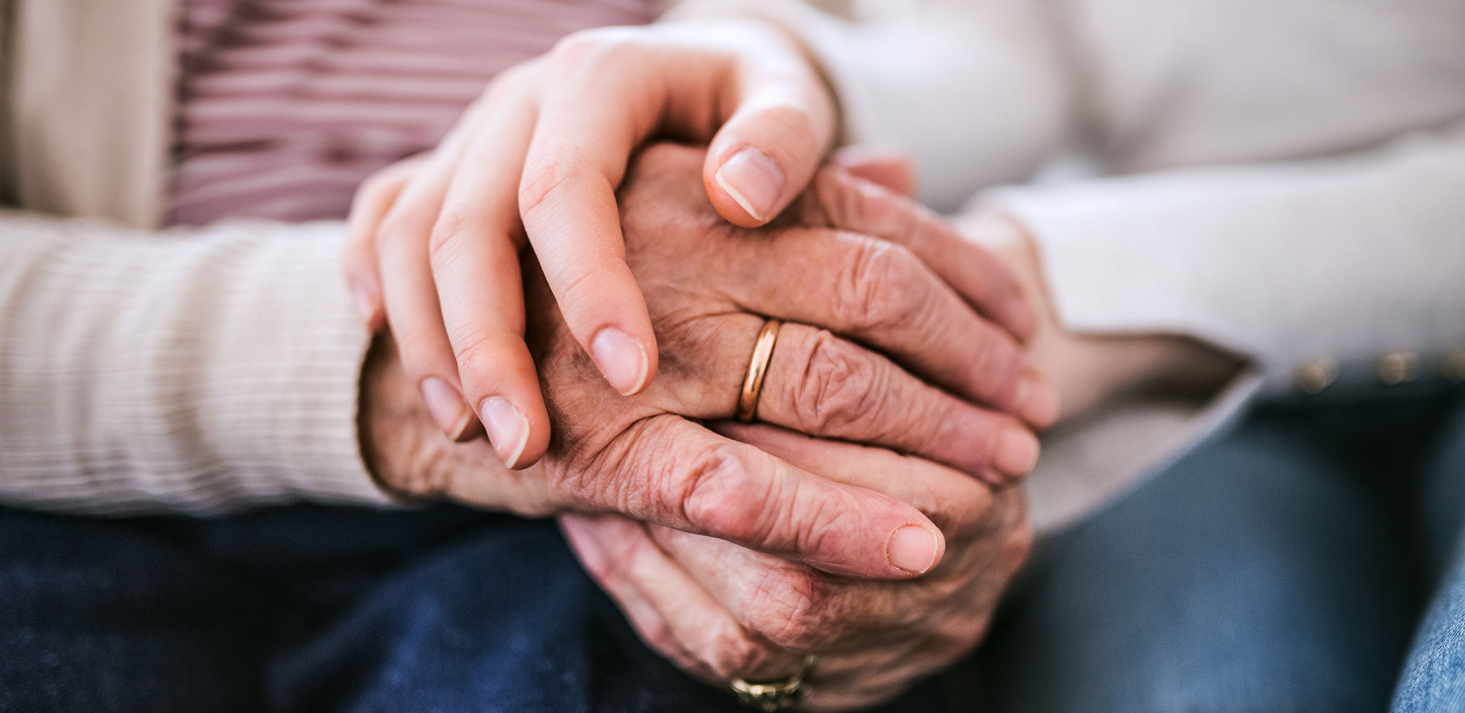 A close up photo of one pair of hands clasping another set of elderly hands