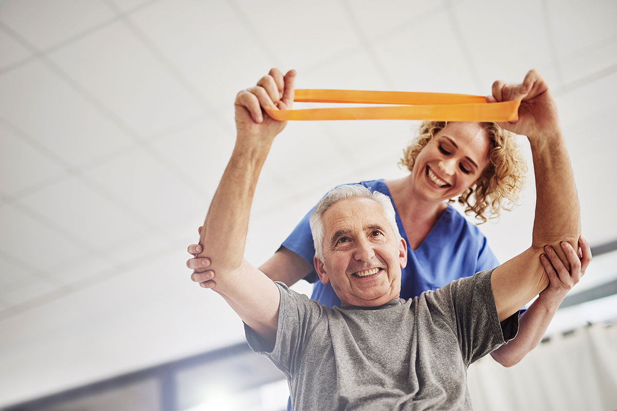 A senior man uses a resistance band with the guidance of a physical therapists